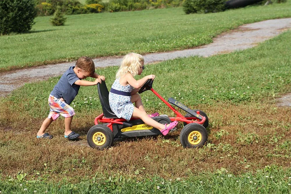 young boy pushing a girl on a pedal cart